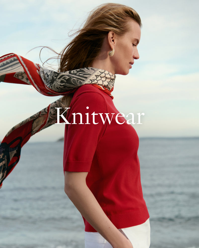 Woman wearing a red knitwear with a patterned scarf by the sea, with 'Knitwear' text overlay.