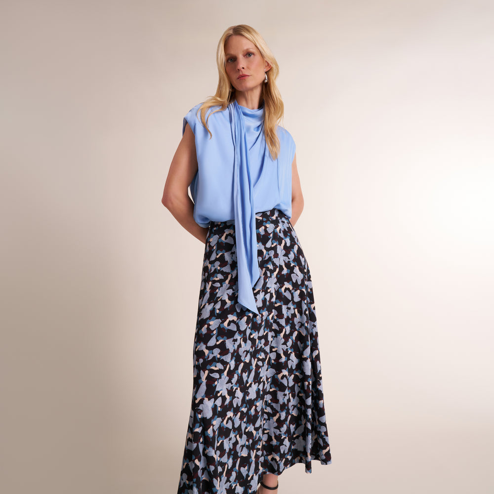 Woman wearing a light blue sleeveless top and a printed skirt on a beige background