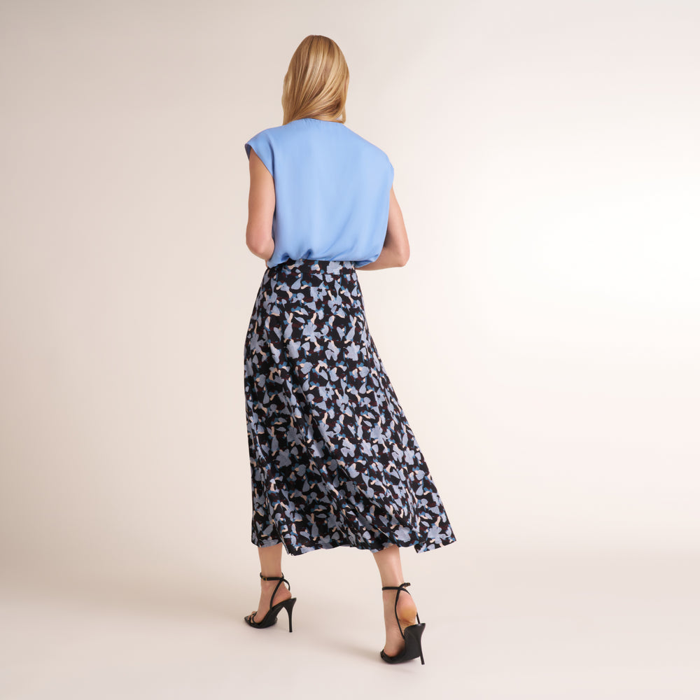 Woman standing wearing a light blue top with a scarf drape neckline and a navy and light blue printed maxi skirt