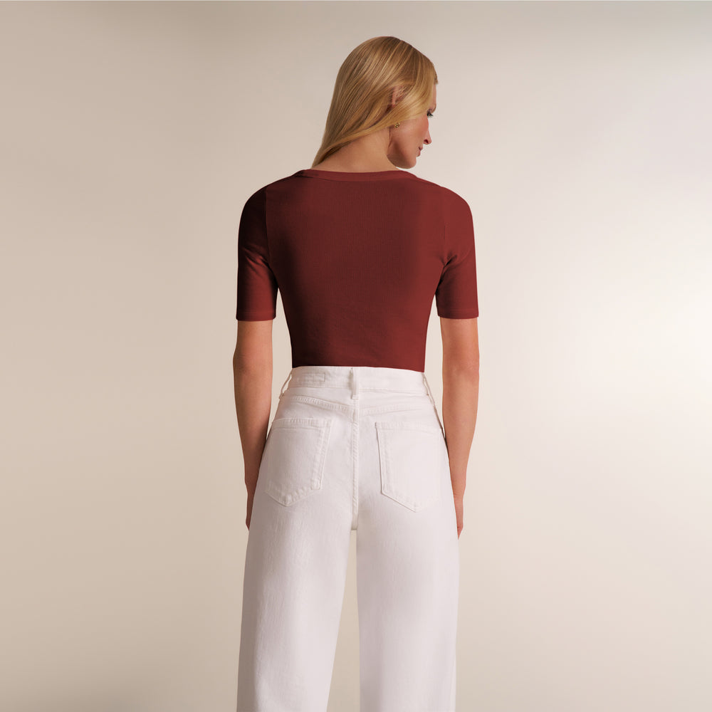 A woman shown from the back wearing a short-sleeve crewneck top in a deep burgundy red and white wide-leg pants, set against a plain beige studio background.