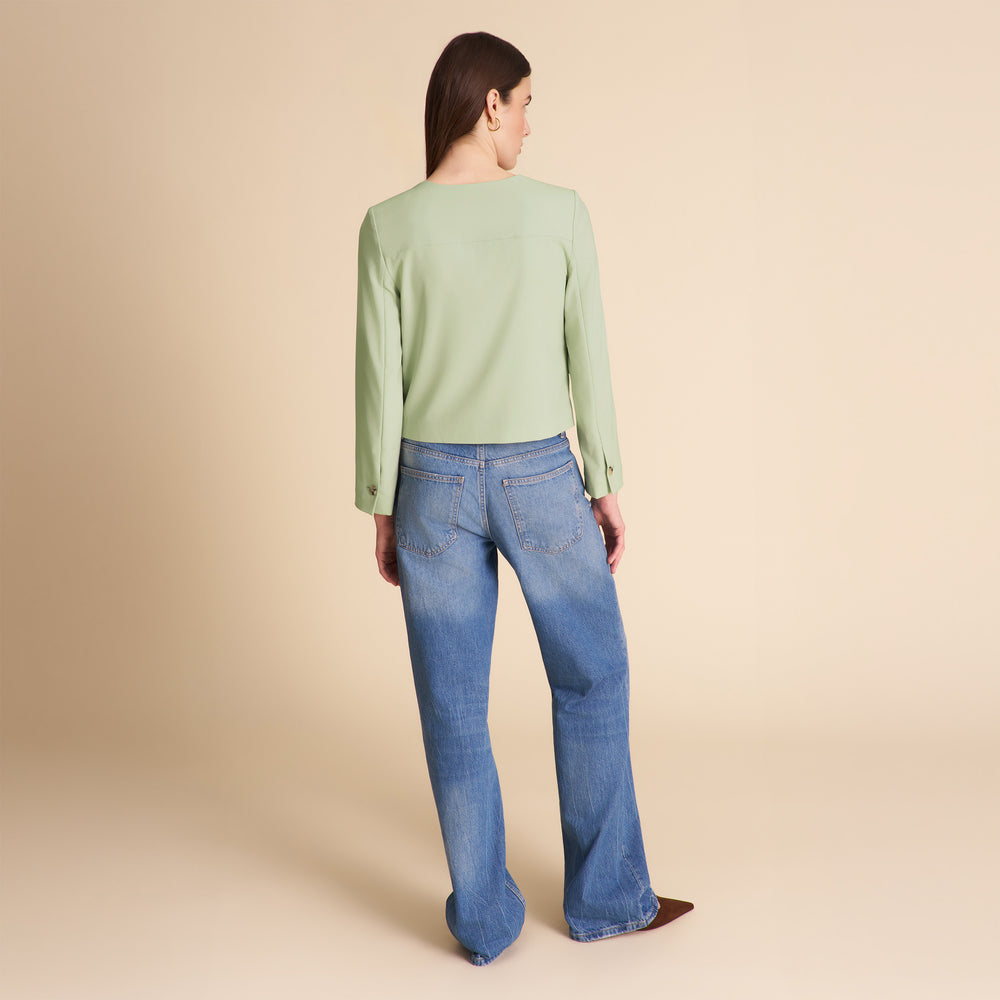 Person wearing a light green sweater and blue jeans on a beige background
