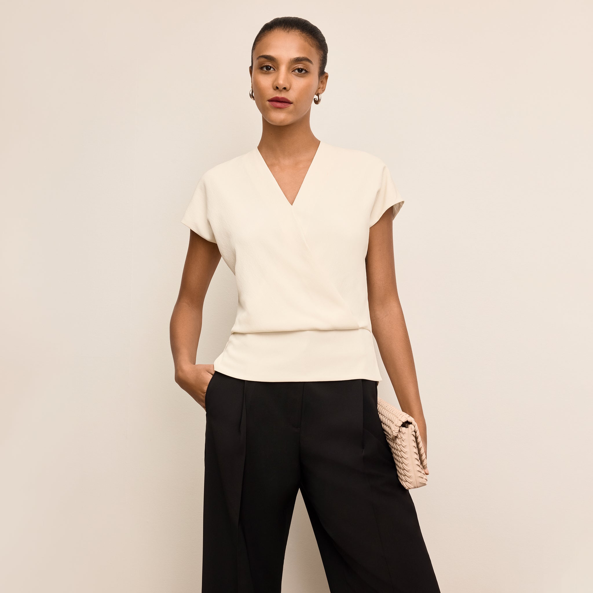 Woman wearing a white top and black pants against a beige background