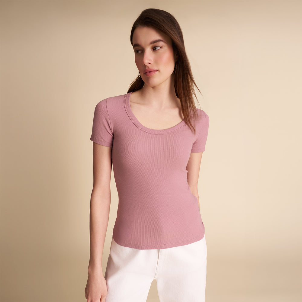 Woman wearing a pink top and white pants against a beige background