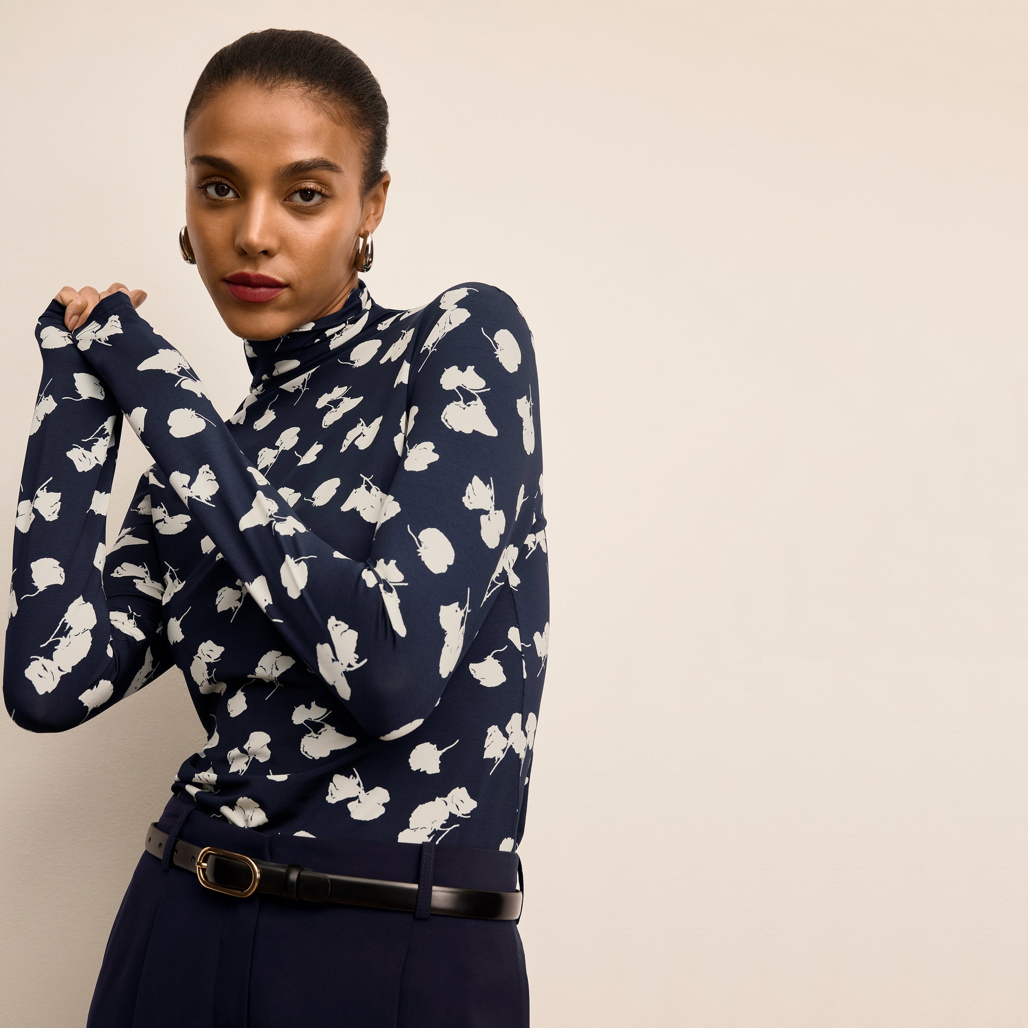 Woman wearing a navy blue sweater with white floral patterns against a beige background