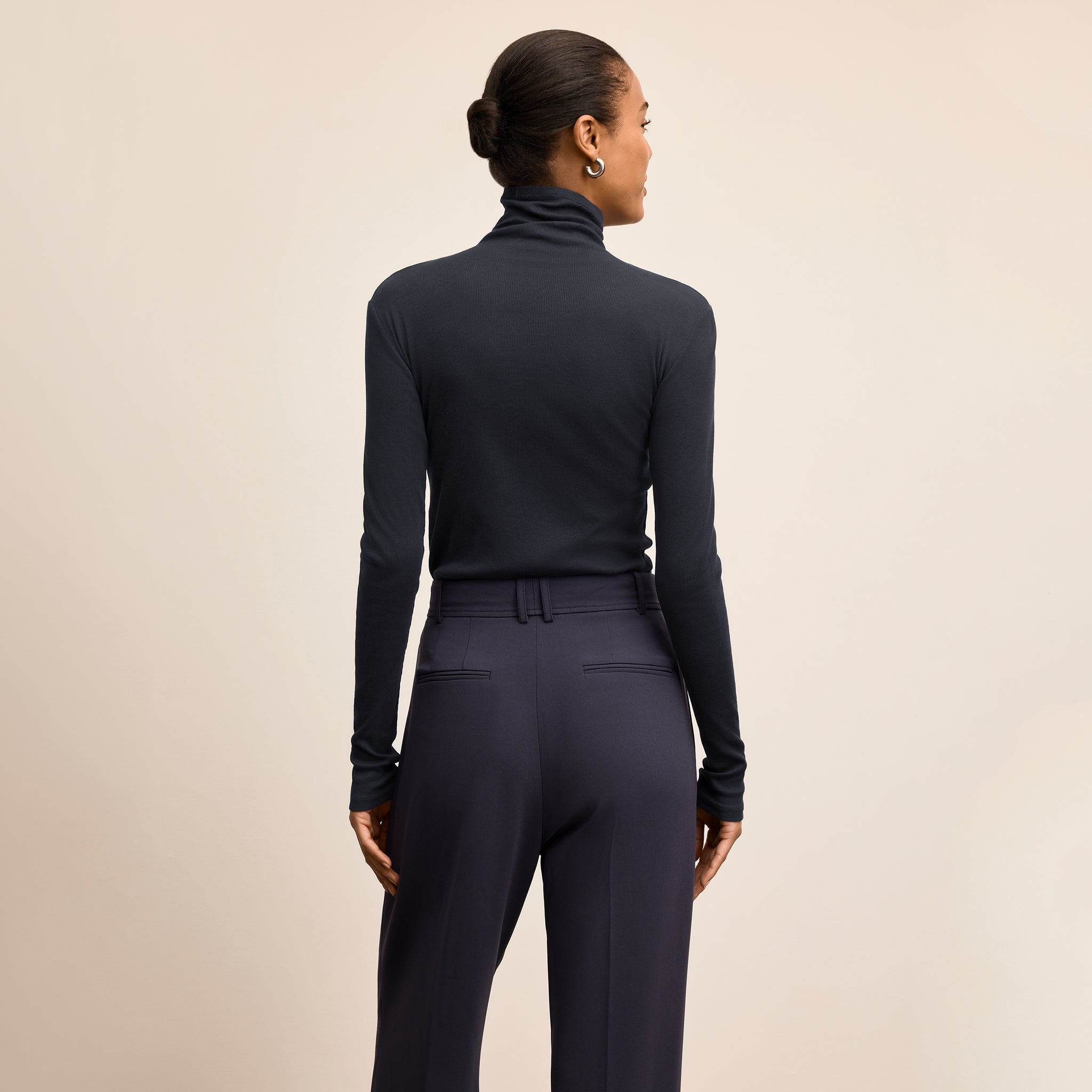 Woman wearing a navy turtleneck and pants against a beige background