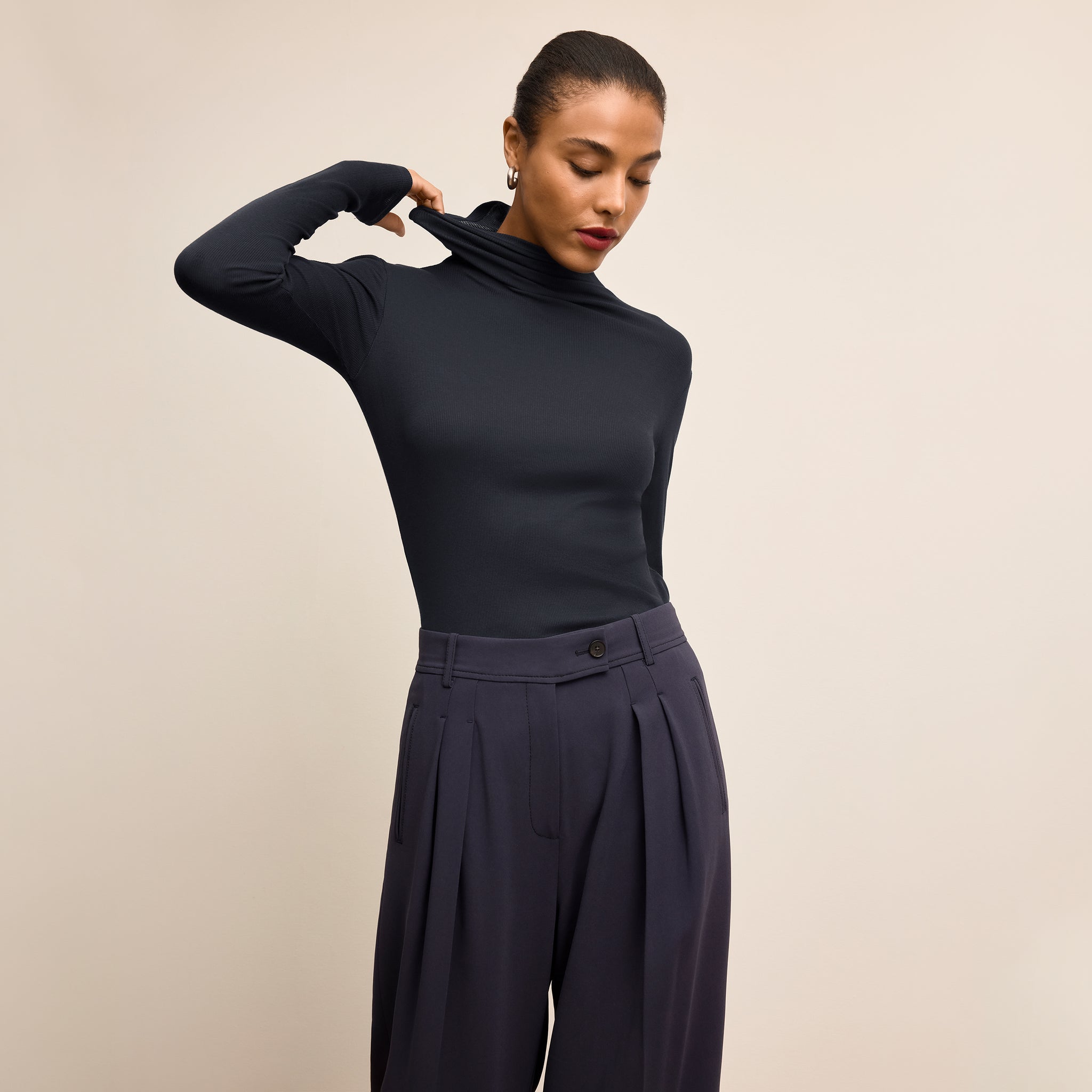 Woman wearing a navy turtleneck and pants against a beige background 