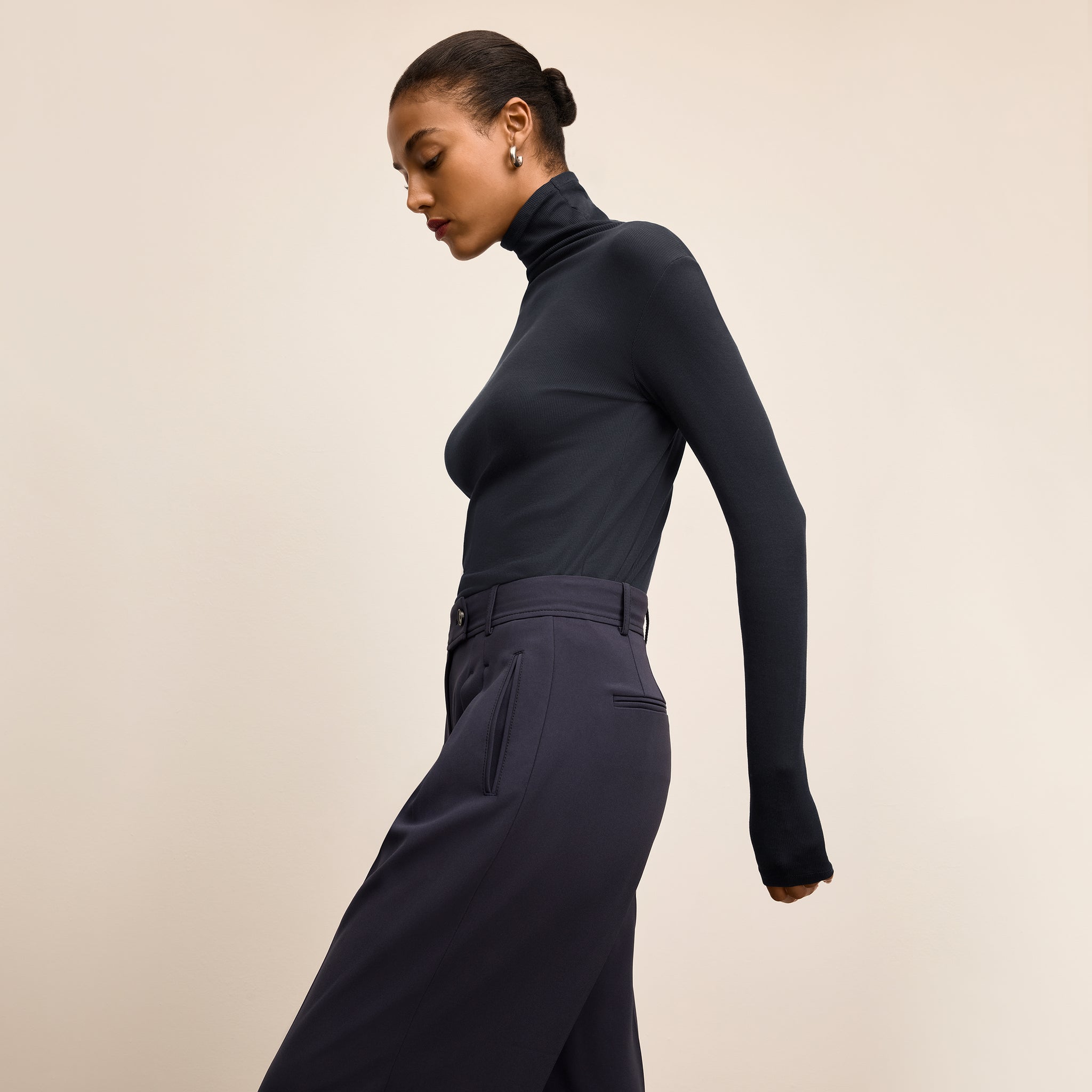 Woman wearing a navy turtleneck and pants against a beige background