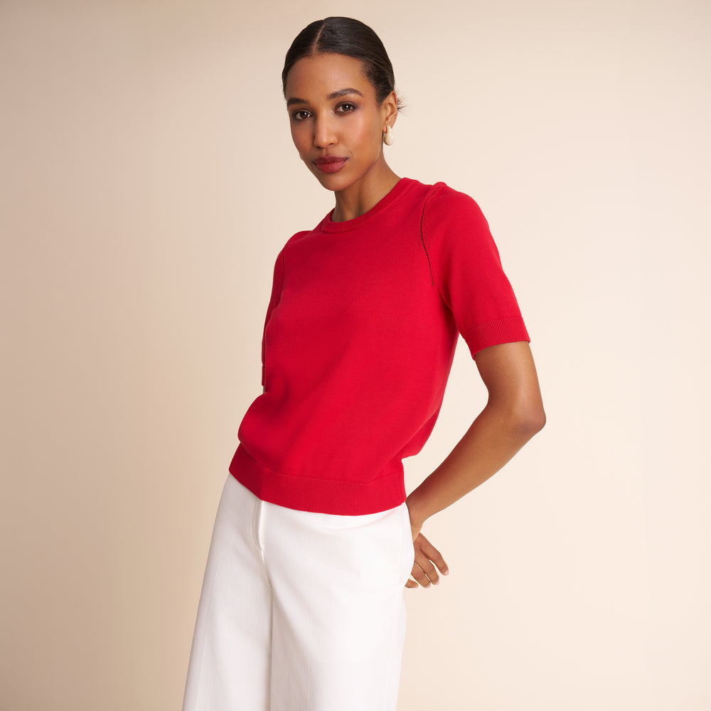 Woman wearing a red top and white pants against a beige background
