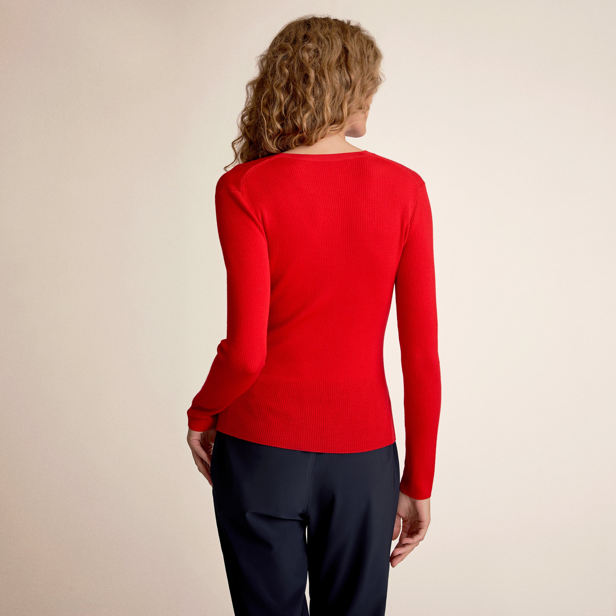 Person wearing a red sweater and black pants on a beige background