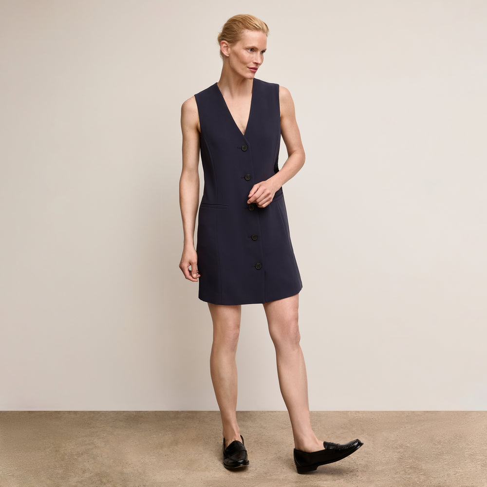 Woman wearing a navy sleeveless dress against a beige background