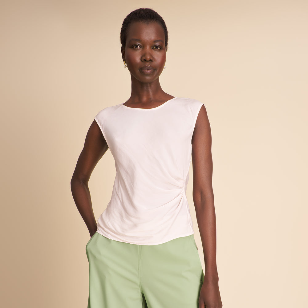 Woman wearing a white sleeveless top and light green pants against a beige background