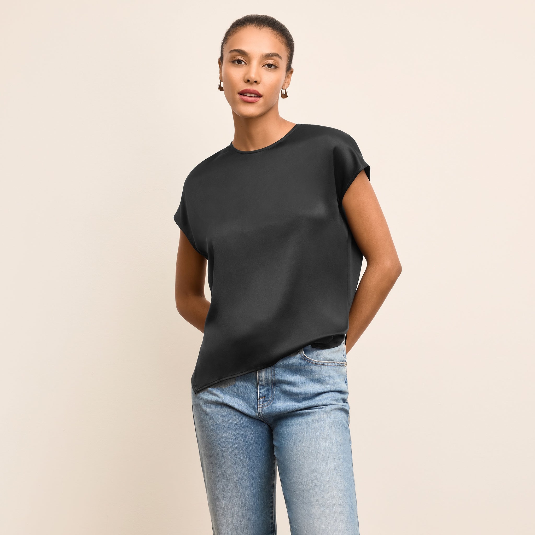 Woman wearing a black top and blue jeans on a beige background 