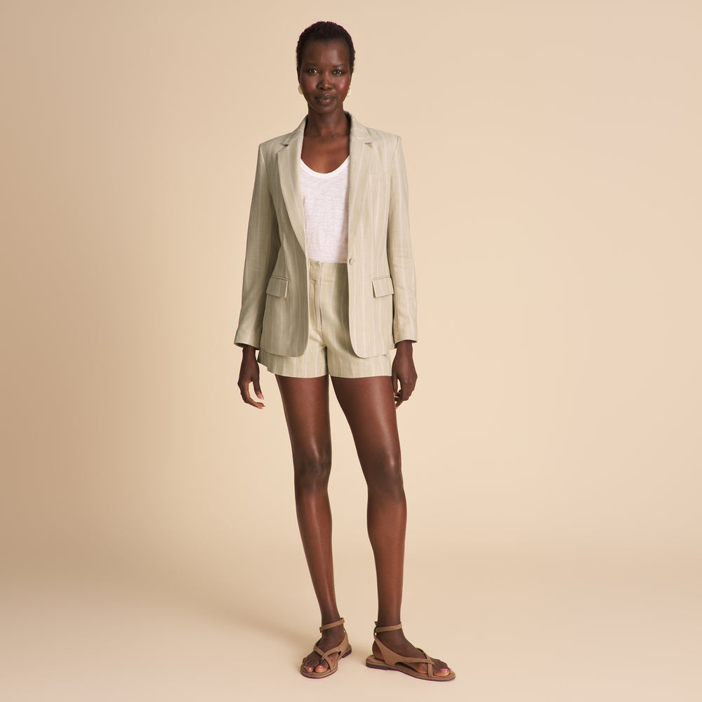 Woman wearing a light green blazer and shorts set on a beige background