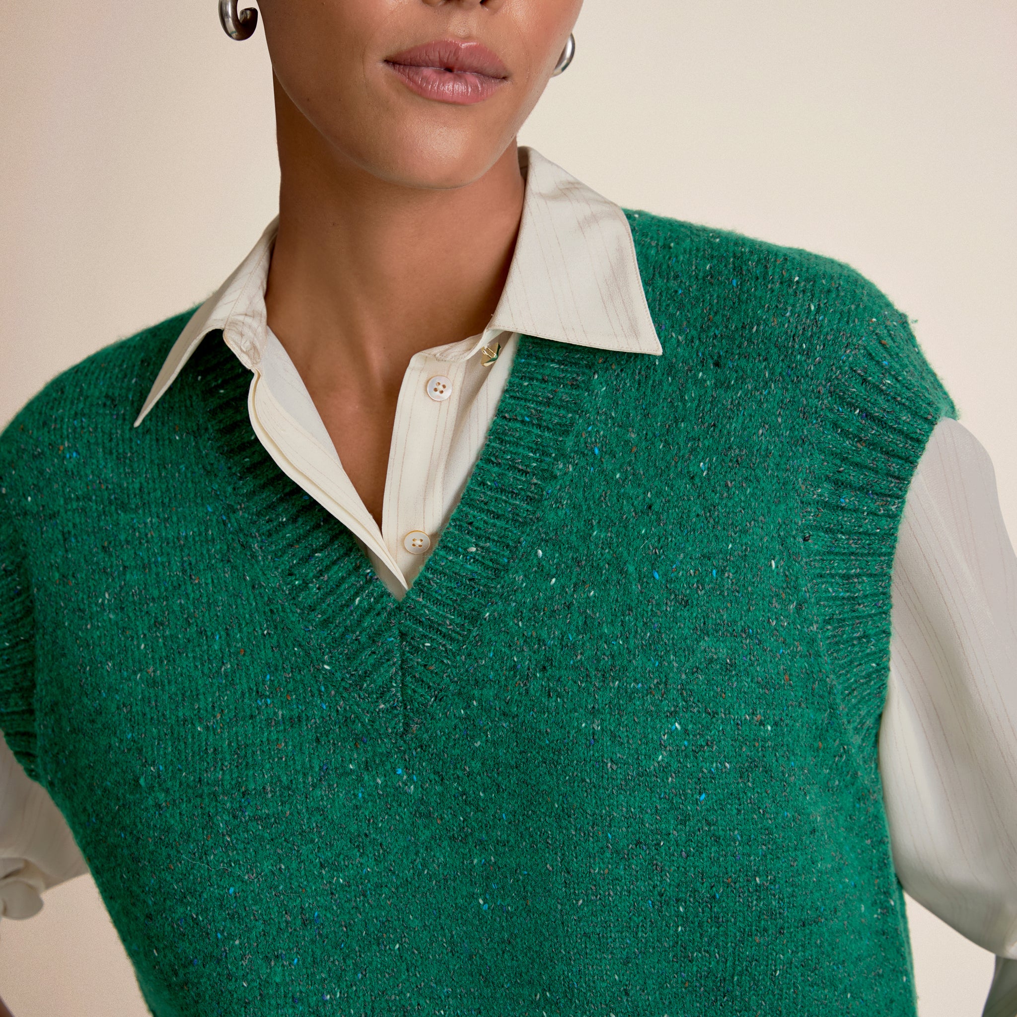 Person wearing a green knitted vest over a white shirt against a neutral background