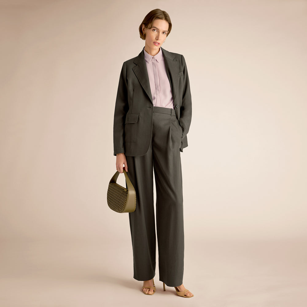 Woman in a gray suit holding a green handbag against a beige background