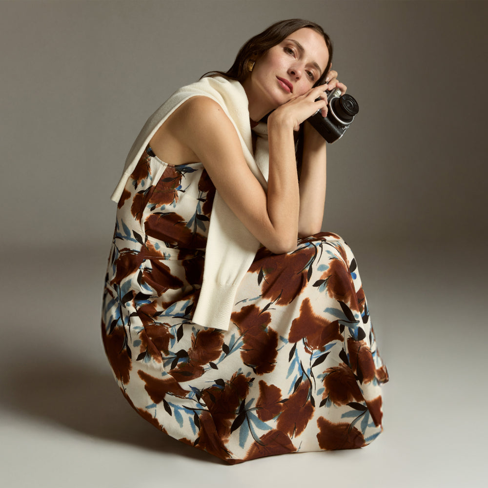 Woman in a floral dress holding a camera against a neutral background