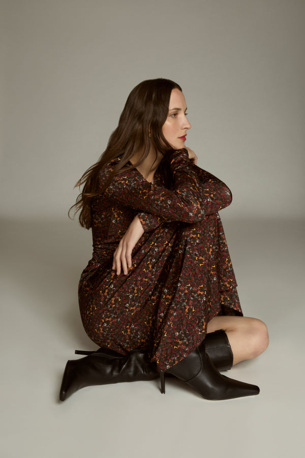 Woman wearing a brown floral dress and black boots on a plain background