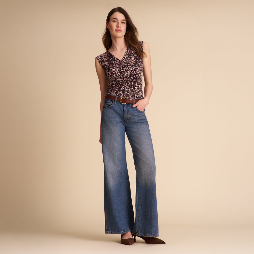 Woman wearing a floral top and blue jeans on a beige background