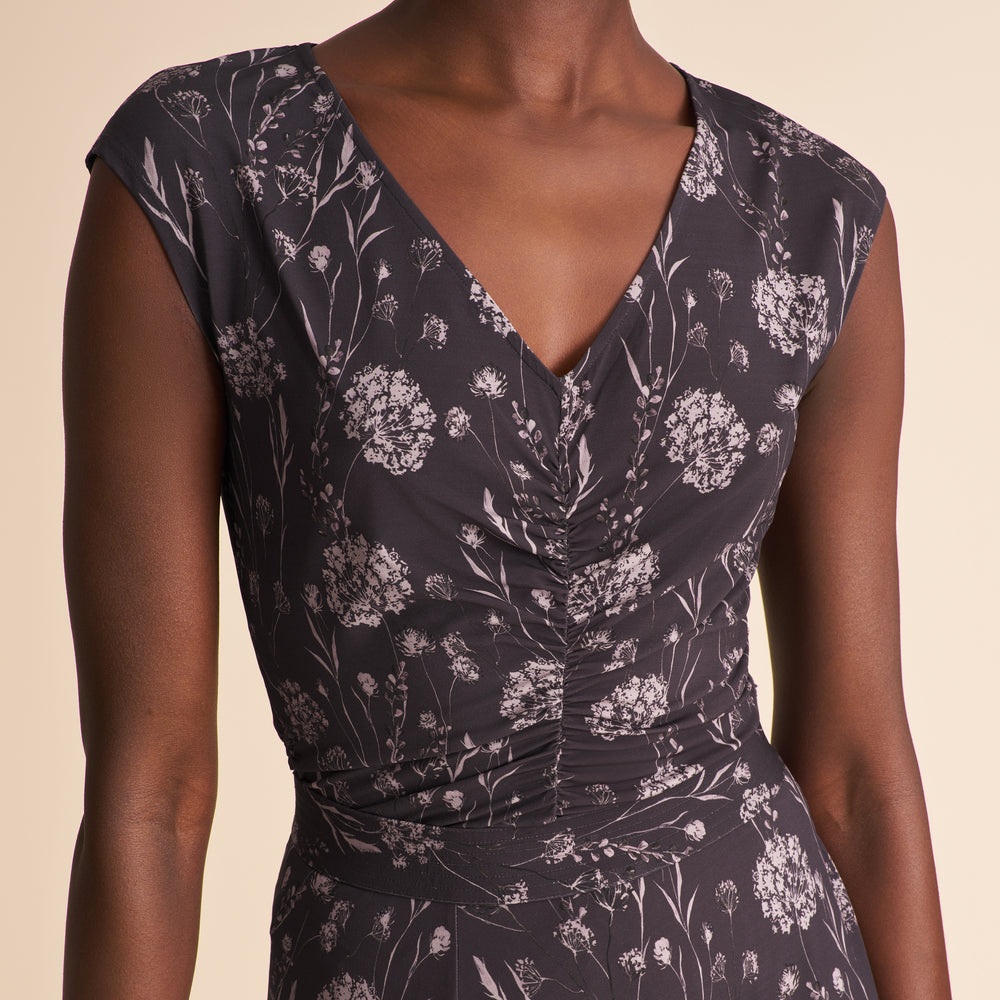 Woman wearing a floral top and white pants against a beige background