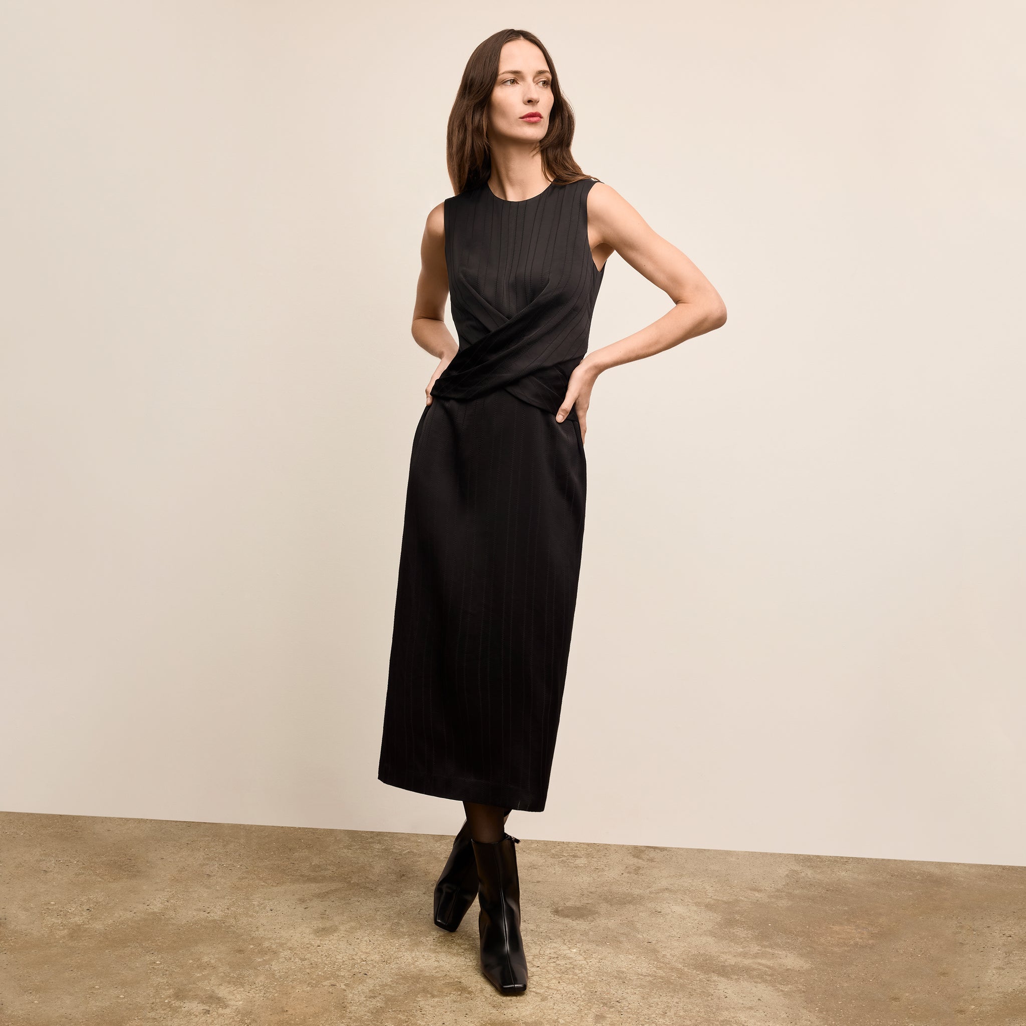Woman wearing a black sleeveless dress against a beige background 