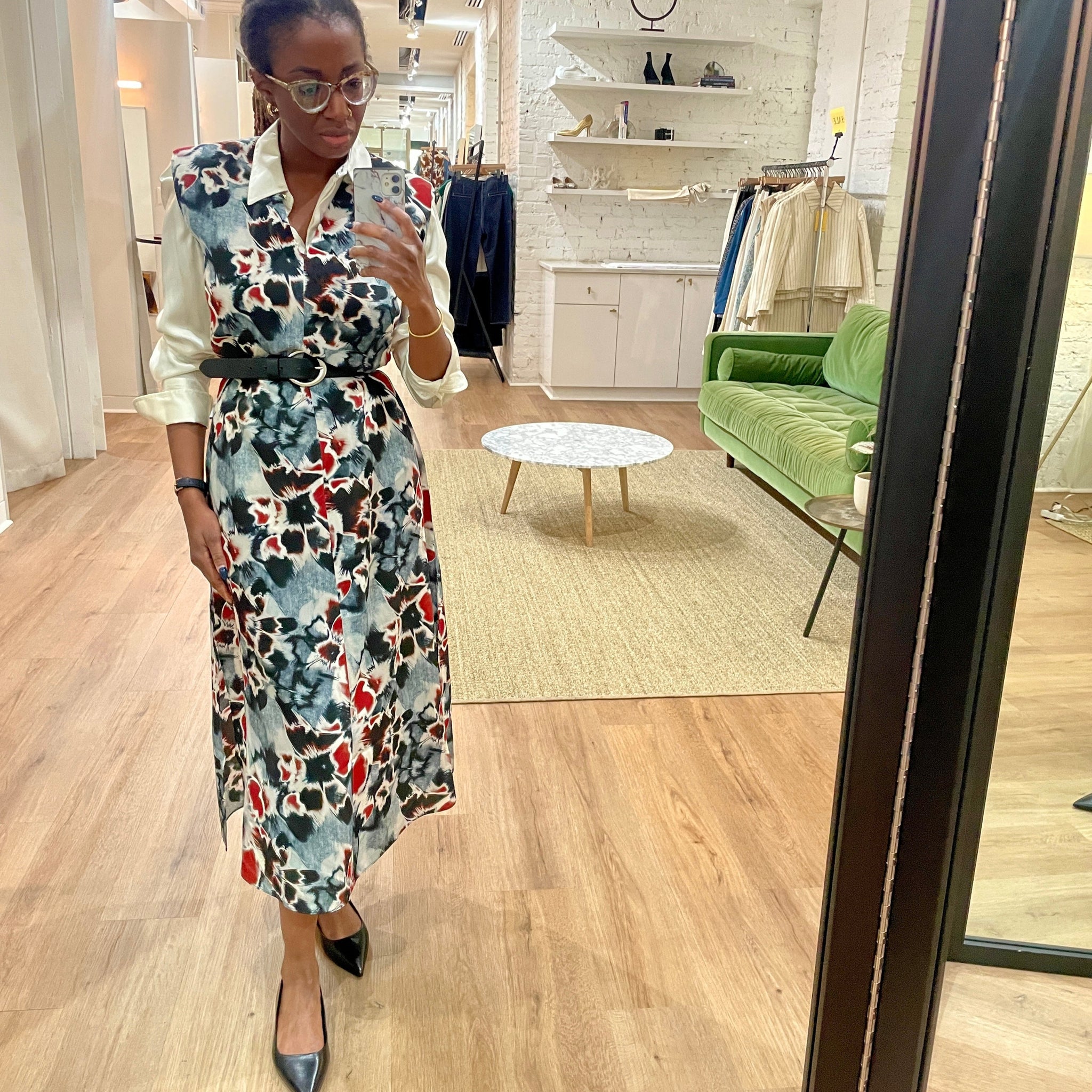 Woman taking a mirror selfie wearing a floral dress in a clothing store.