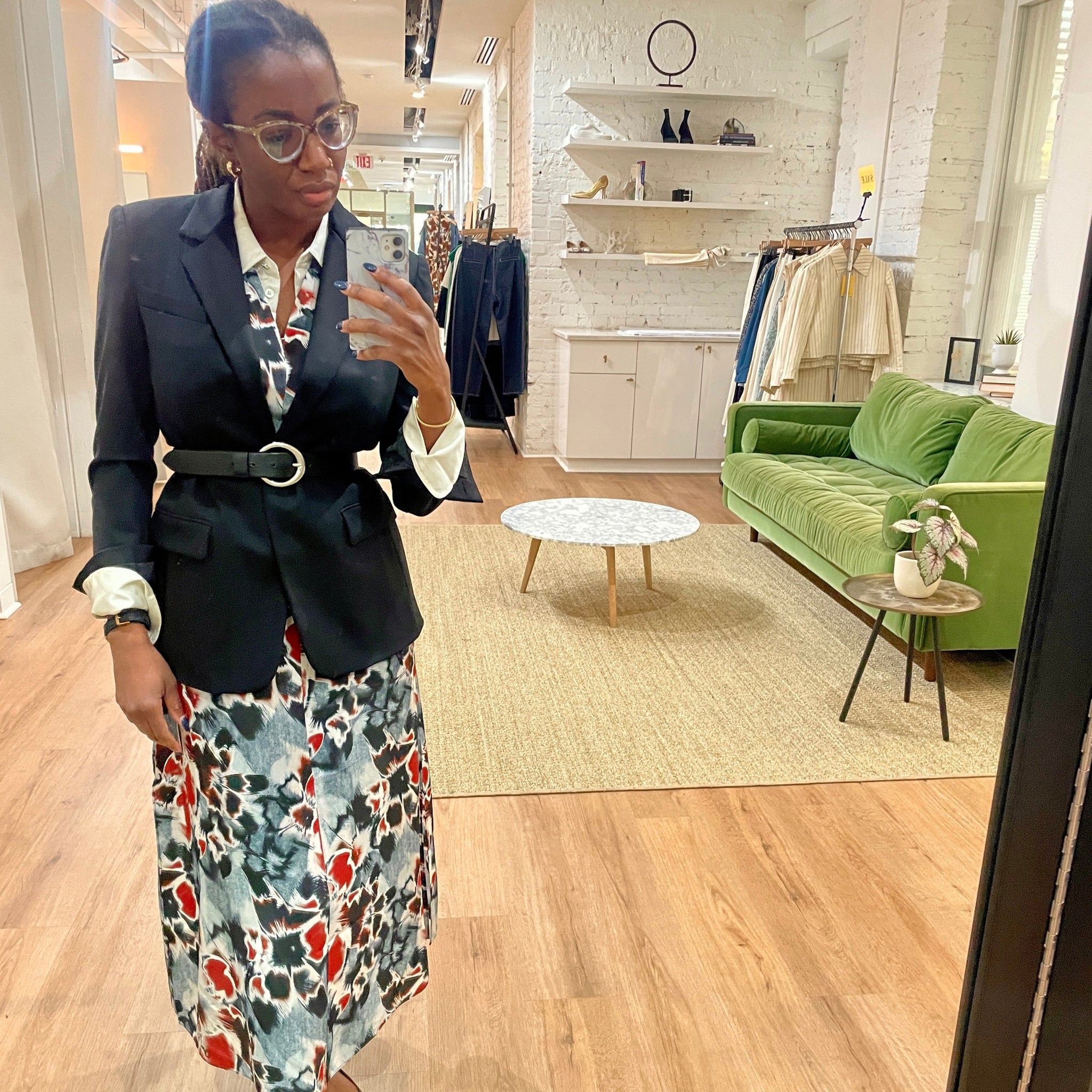Woman taking a mirror selfie in a store wearing a blazer and floral dress. 