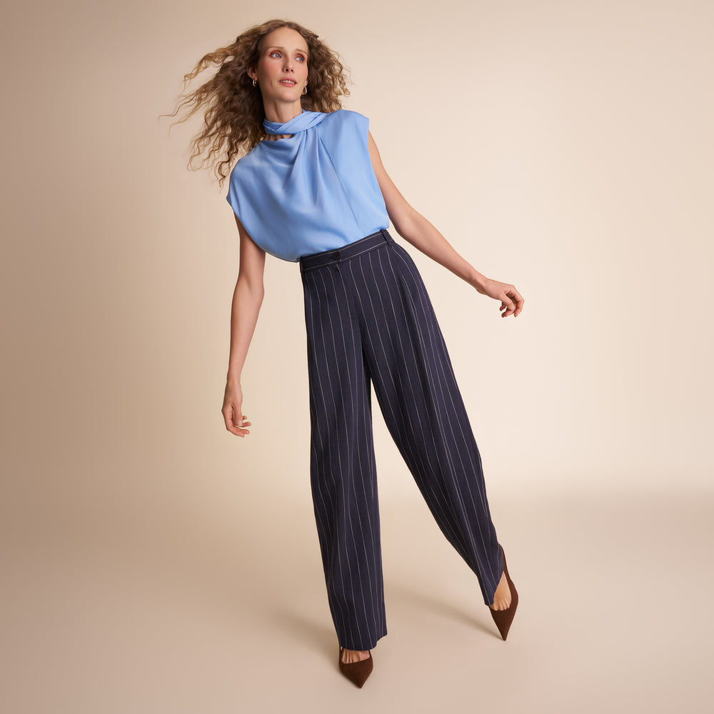 Woman wearing a light blue sleeveless top and dark pinstripe pants on a beige background