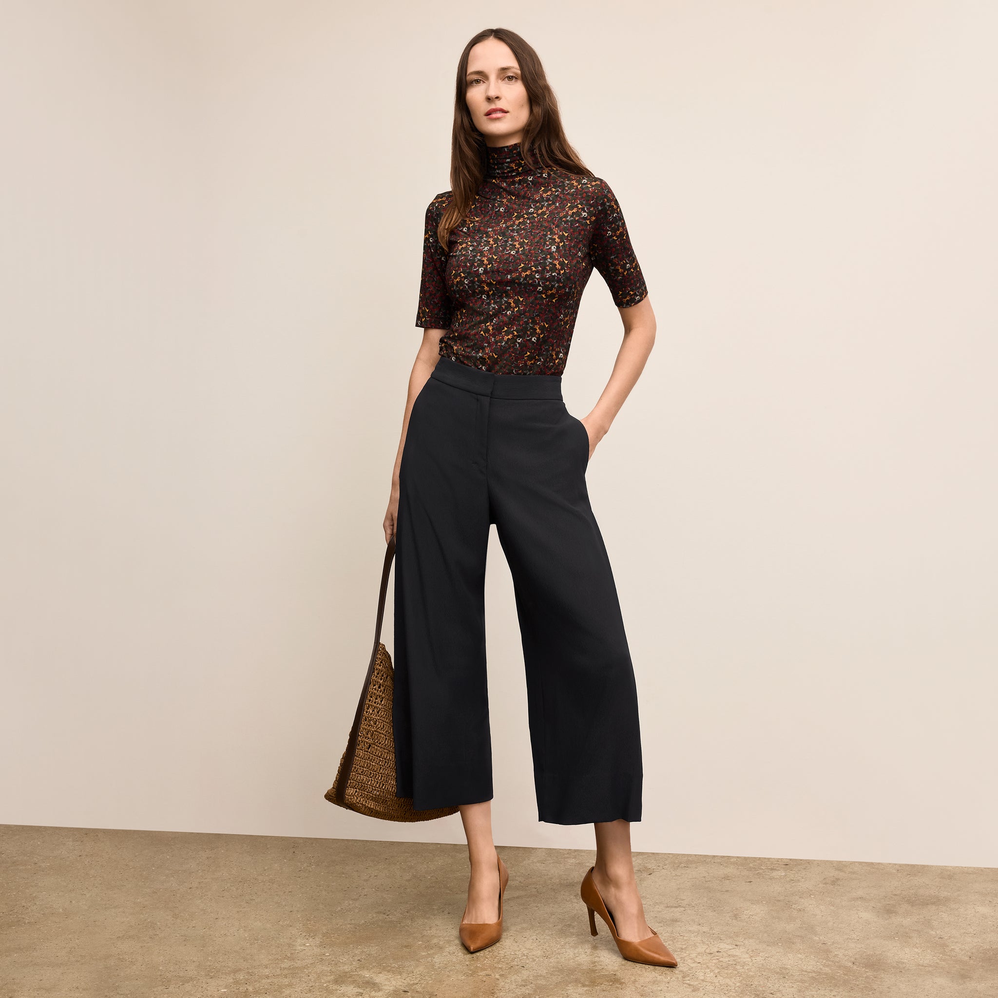 Woman wearing a patterned top and black wide-leg pants on a beige background