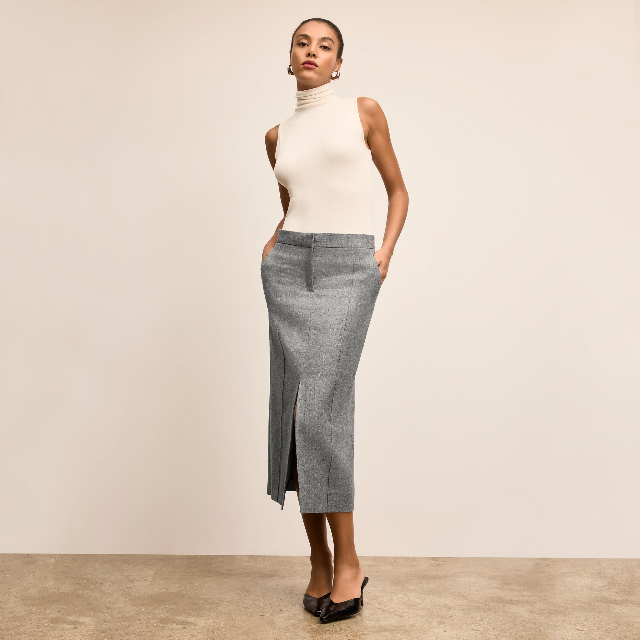 Woman wearing a white turtleneck top and gray skirt against a beige background