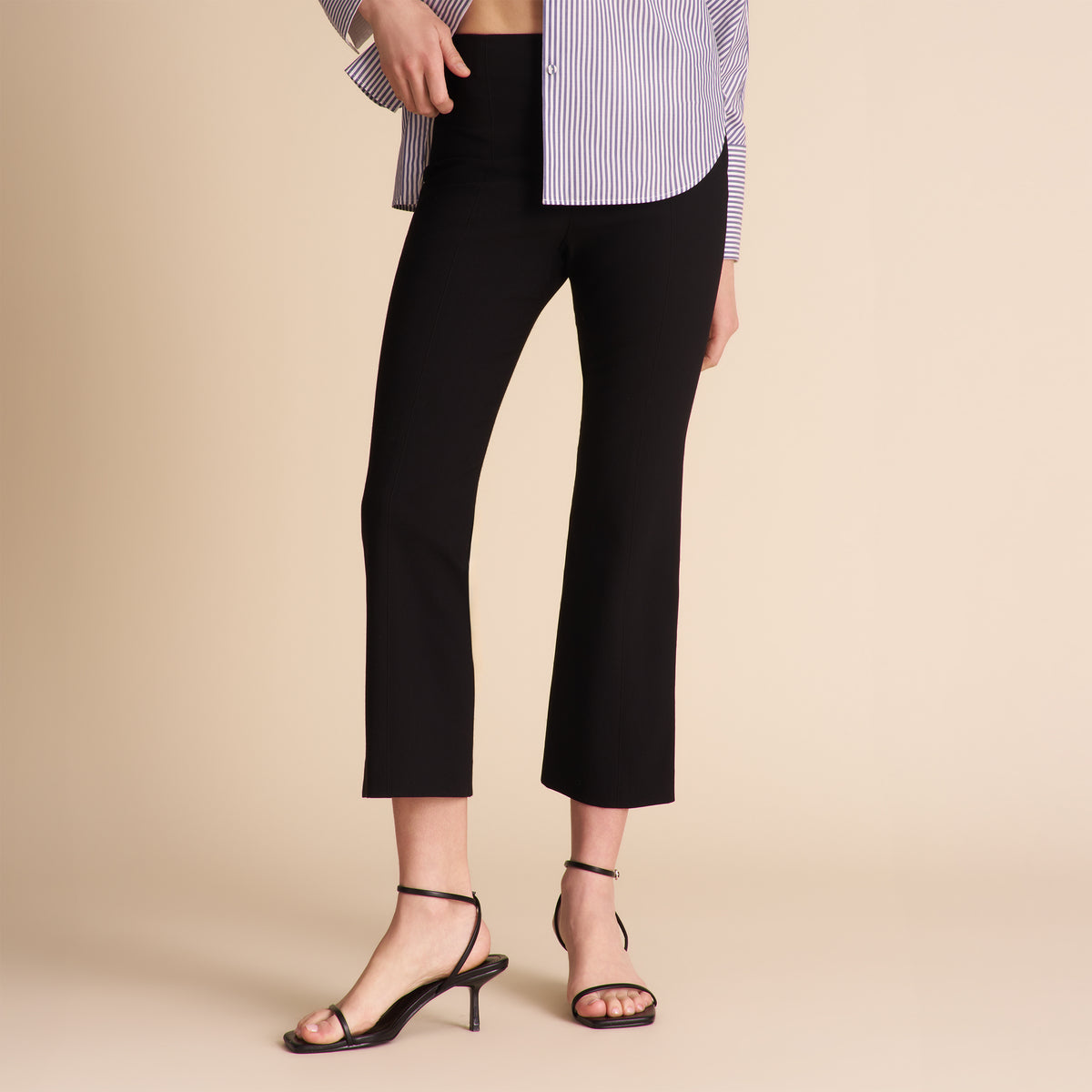 Person wearing black pants and a striped shirt on a beige background