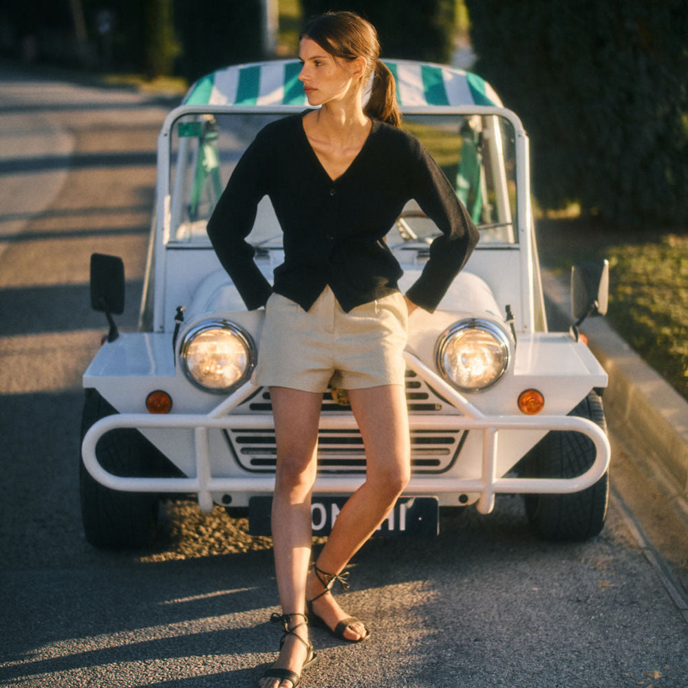 Woman standing in front of a small white vehicle with a green and white striped roof on a road.