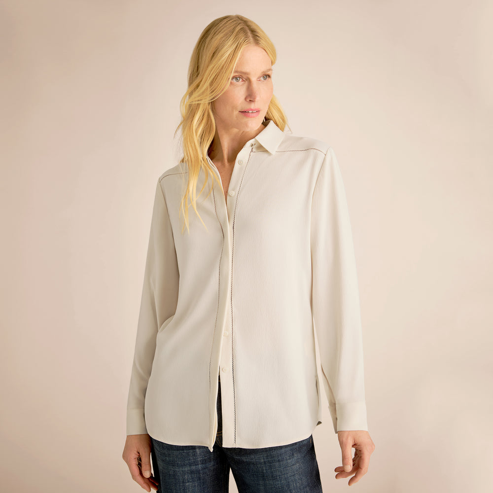 Woman wearing a light-colored shirt and dark jeans against a beige background