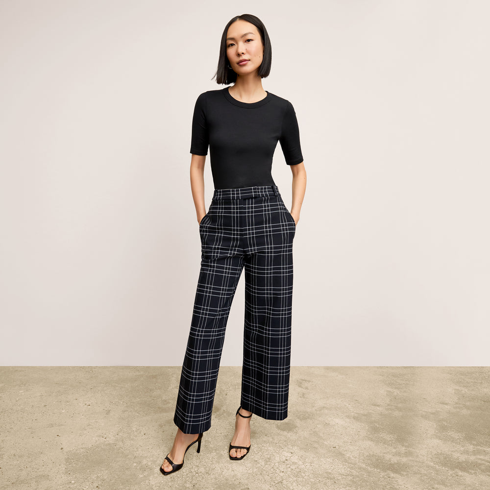 Woman wearing a black top and plaid pants against a plain background