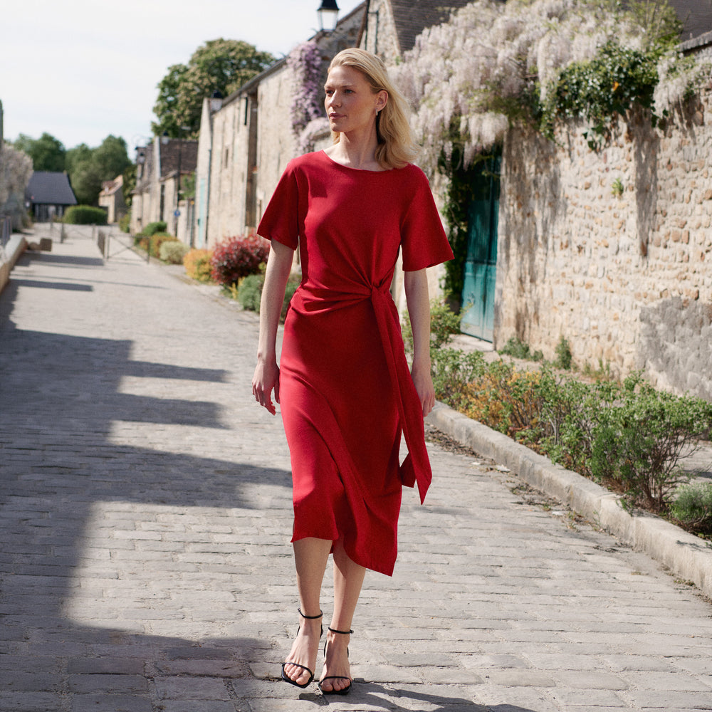 Woman in a red dress walking on a stone path in a quaint village.