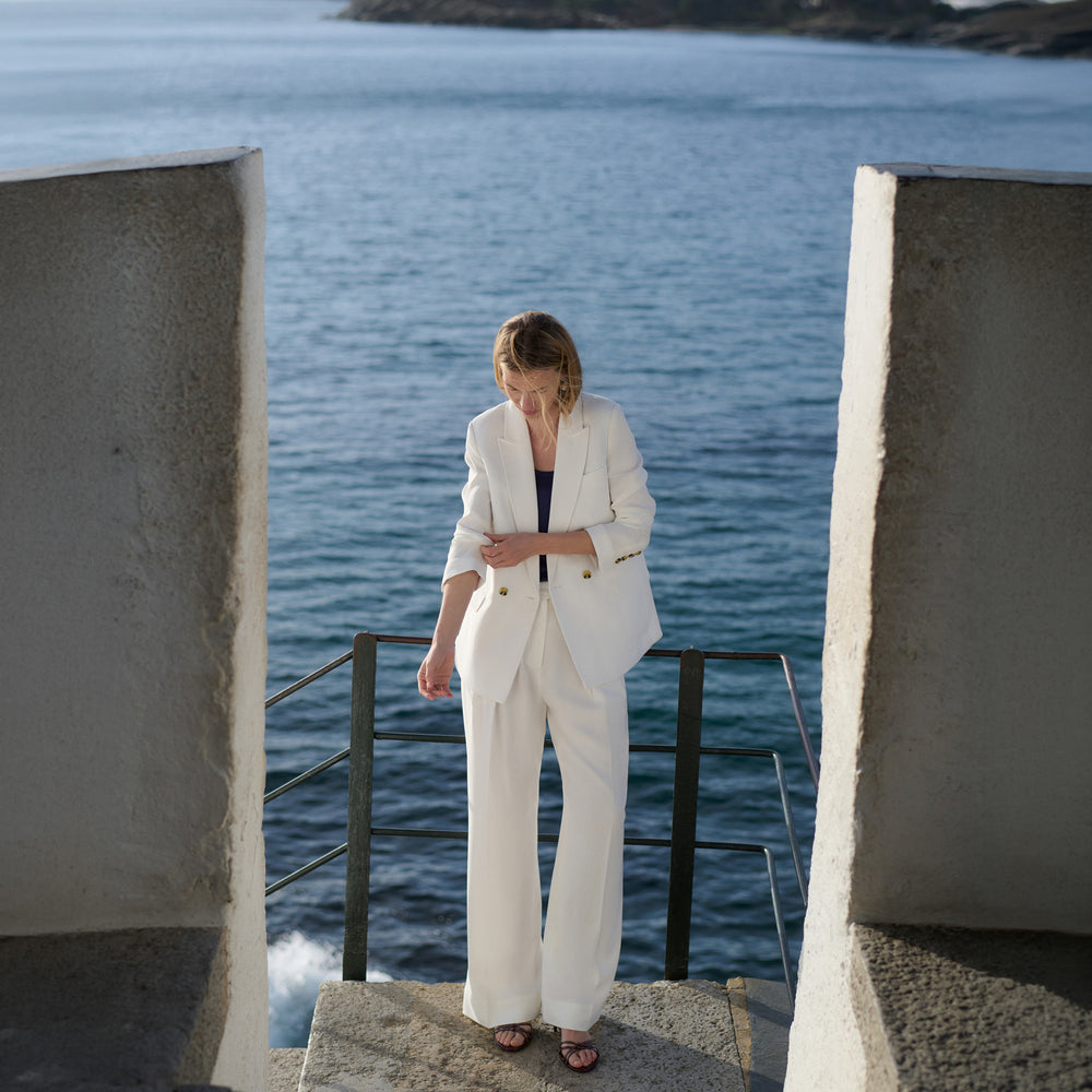 Woman in a white suit standing by a body of water with concrete structures.