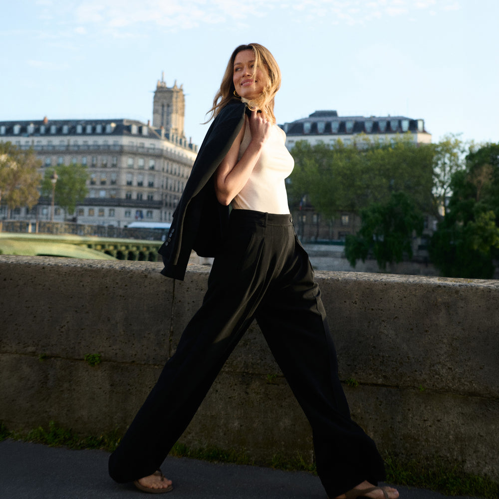 Woman in a cream top and black pants standing on a bridge with a cityscape background