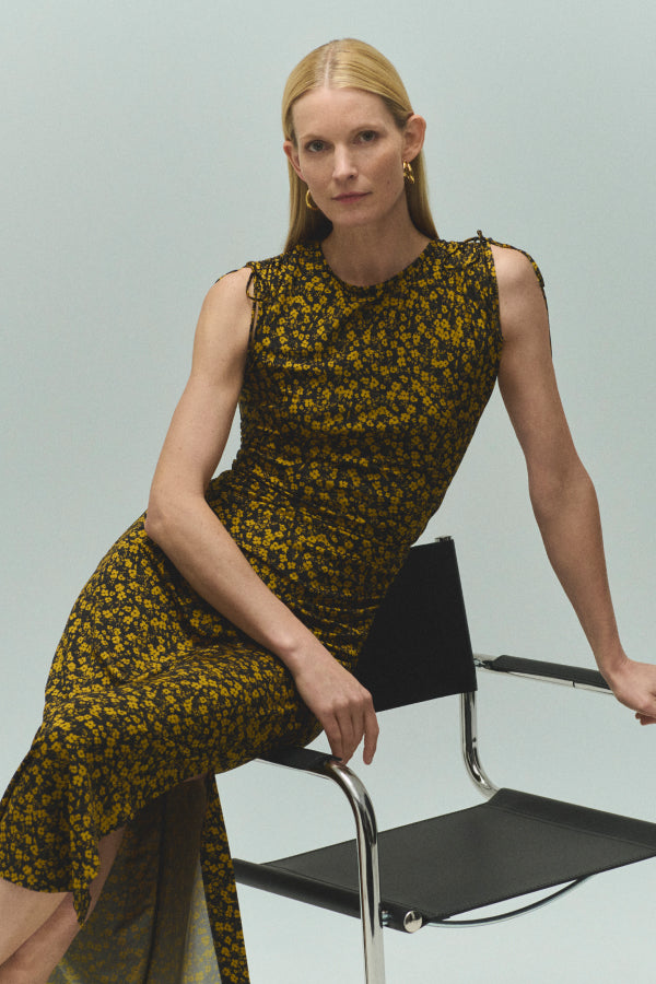 Woman in a floral dress sitting on a chair against a light gray background