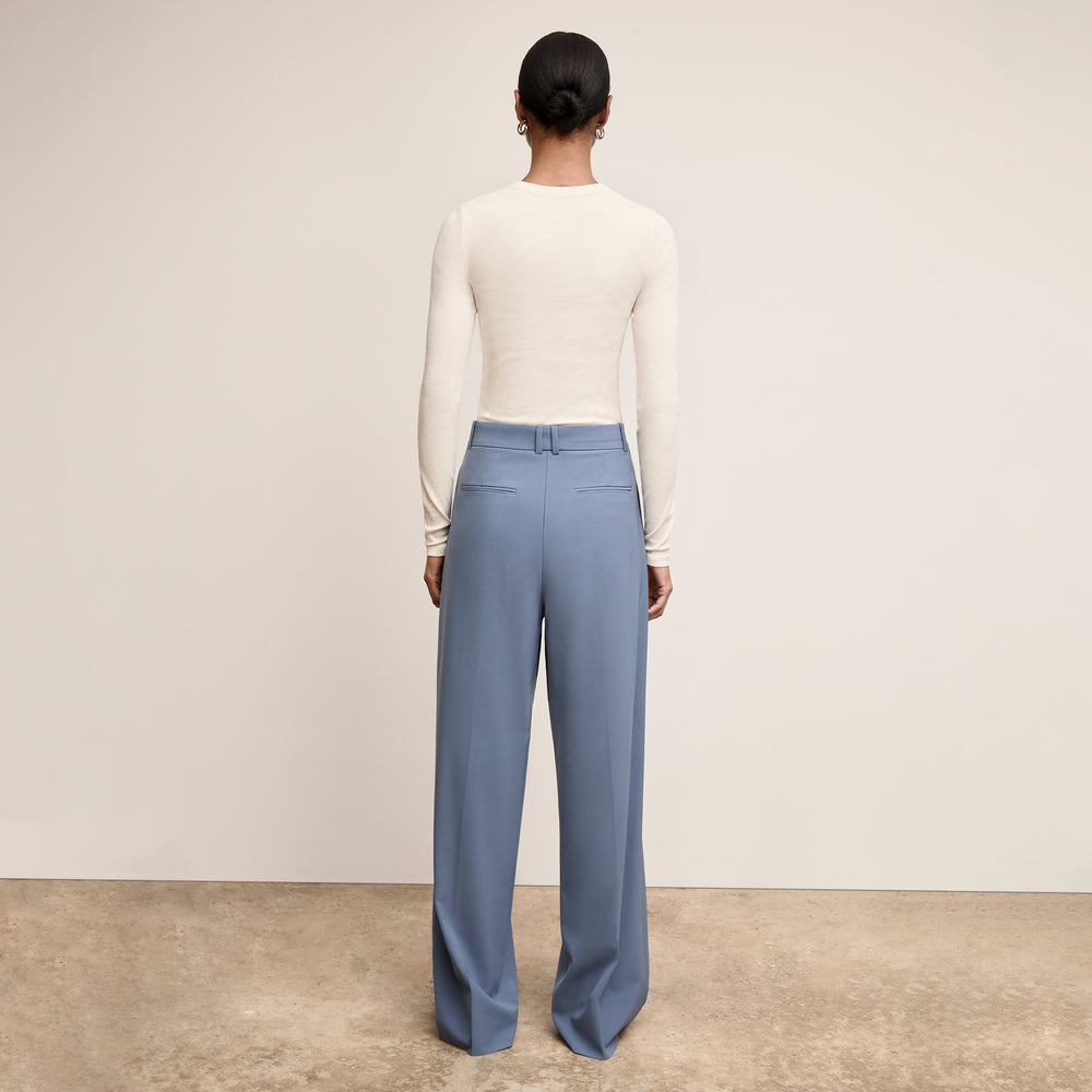 Woman wearing a white long-sleeve top and blue pants against a plain background