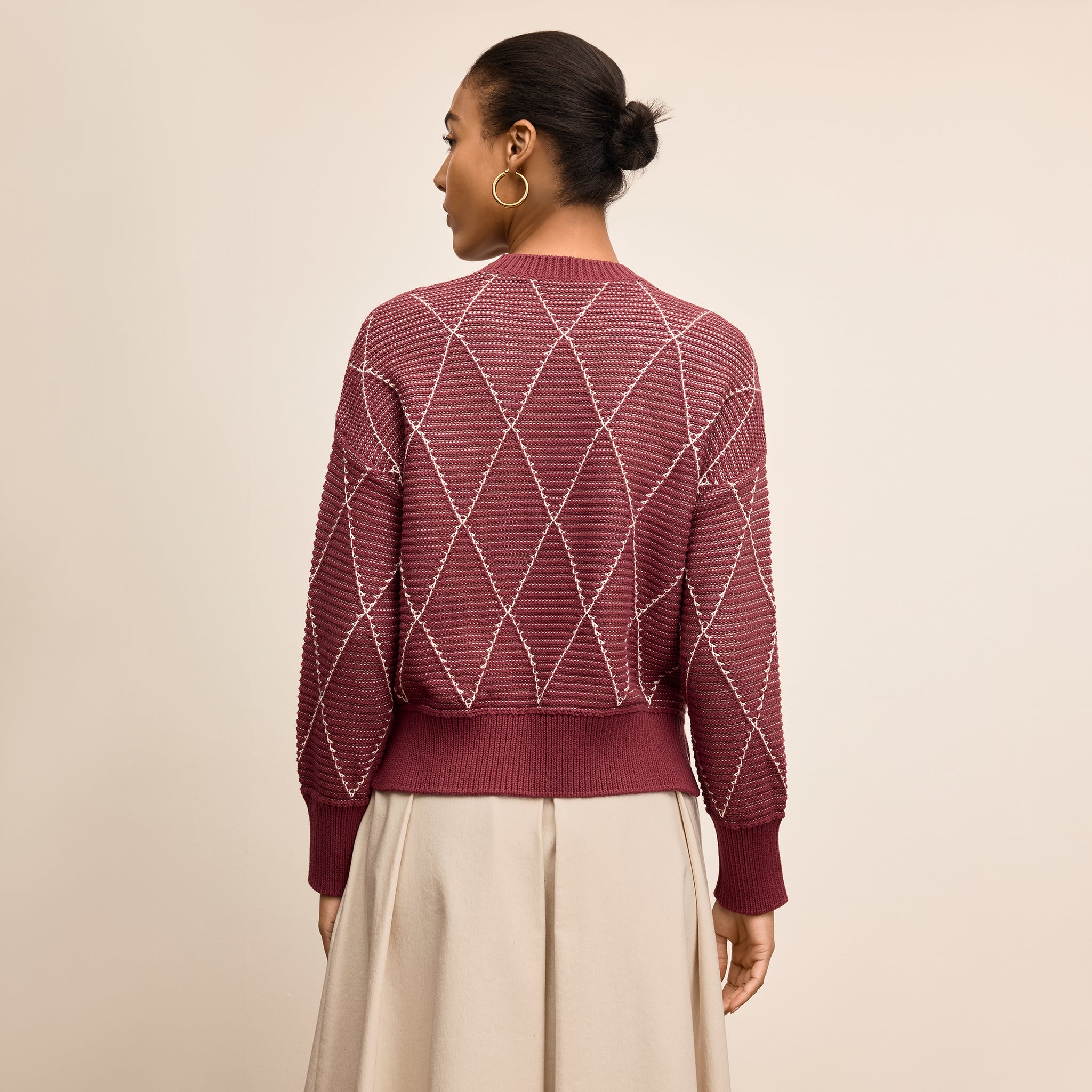 Woman wearing a maroon sweater with a geometric pattern on a beige background