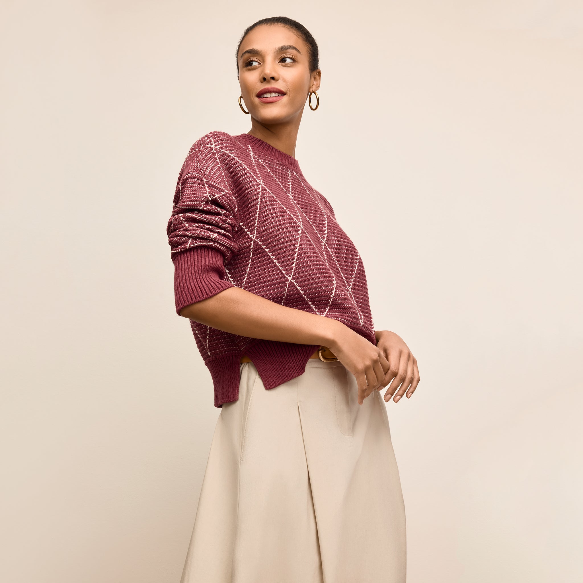 Woman wearing a maroon sweater with a geometric pattern on a beige background