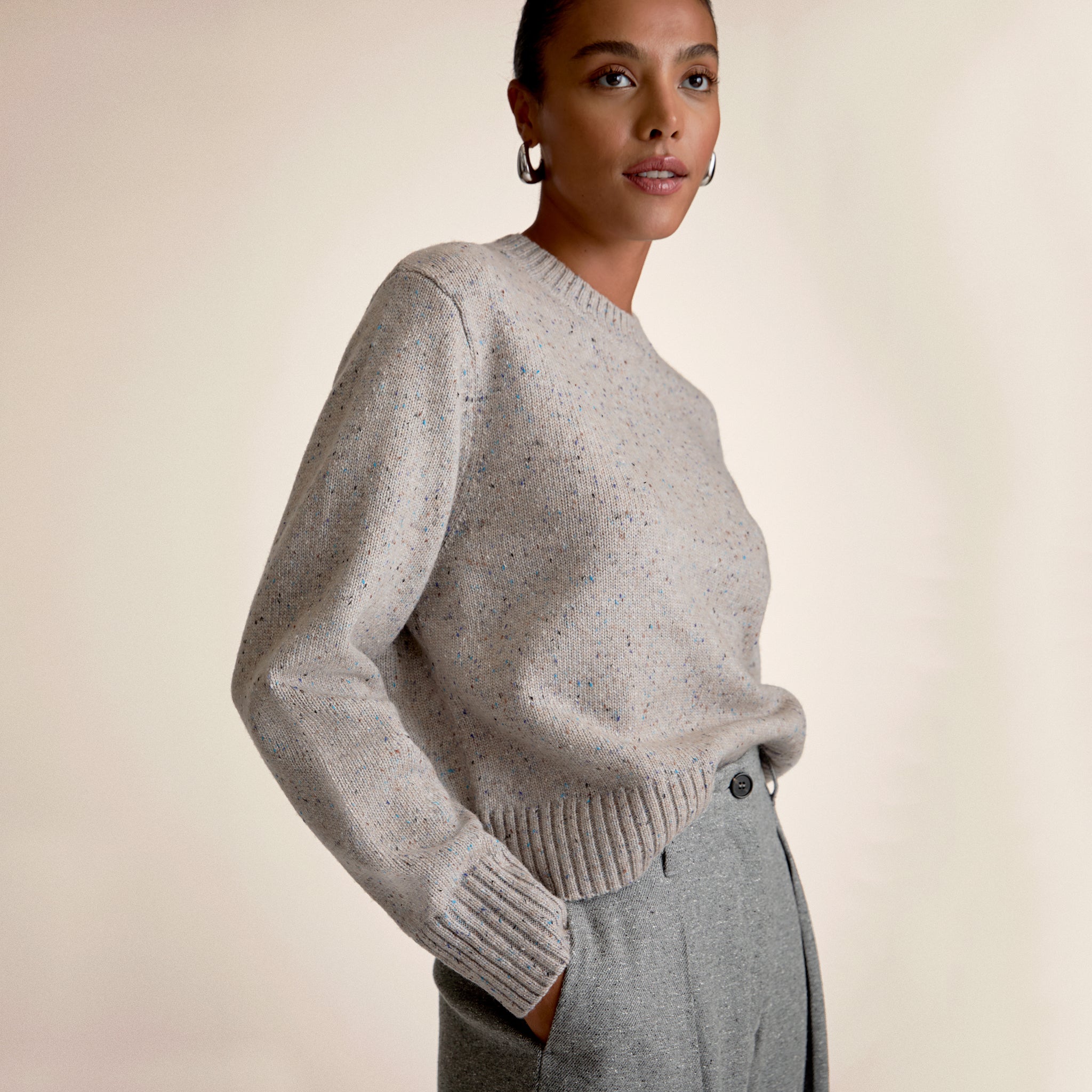 Woman wearing a gray sweater and pants against a beige background 