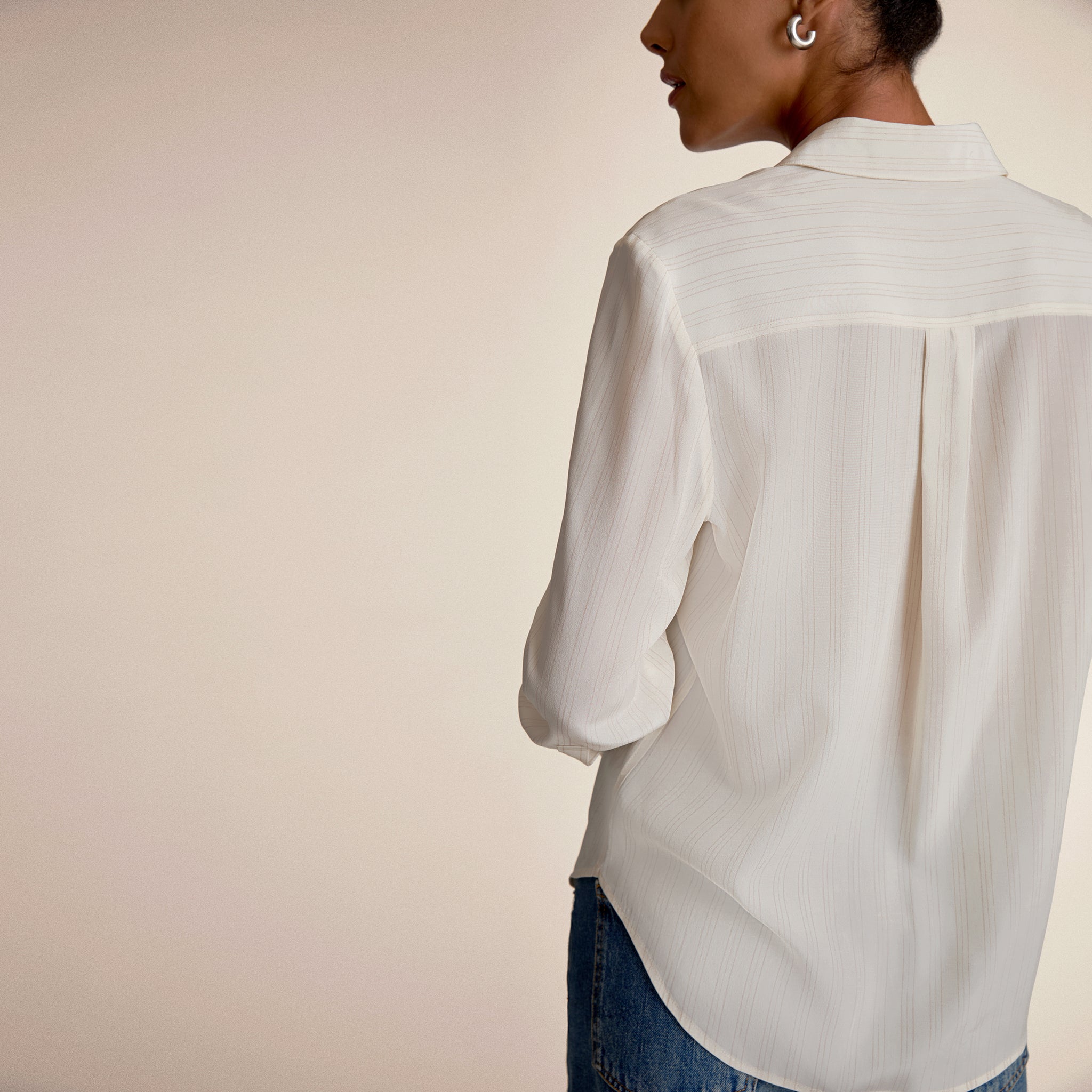 Person wearing a light-colored shirt and jeans against a plain background