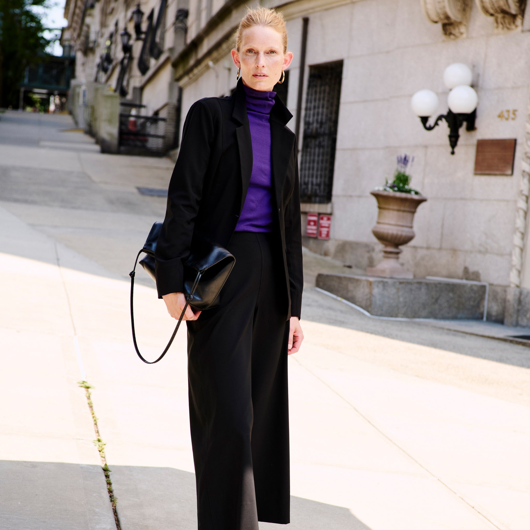 Front image of a woman standing wearing the moreland jacket--origami suiting in black