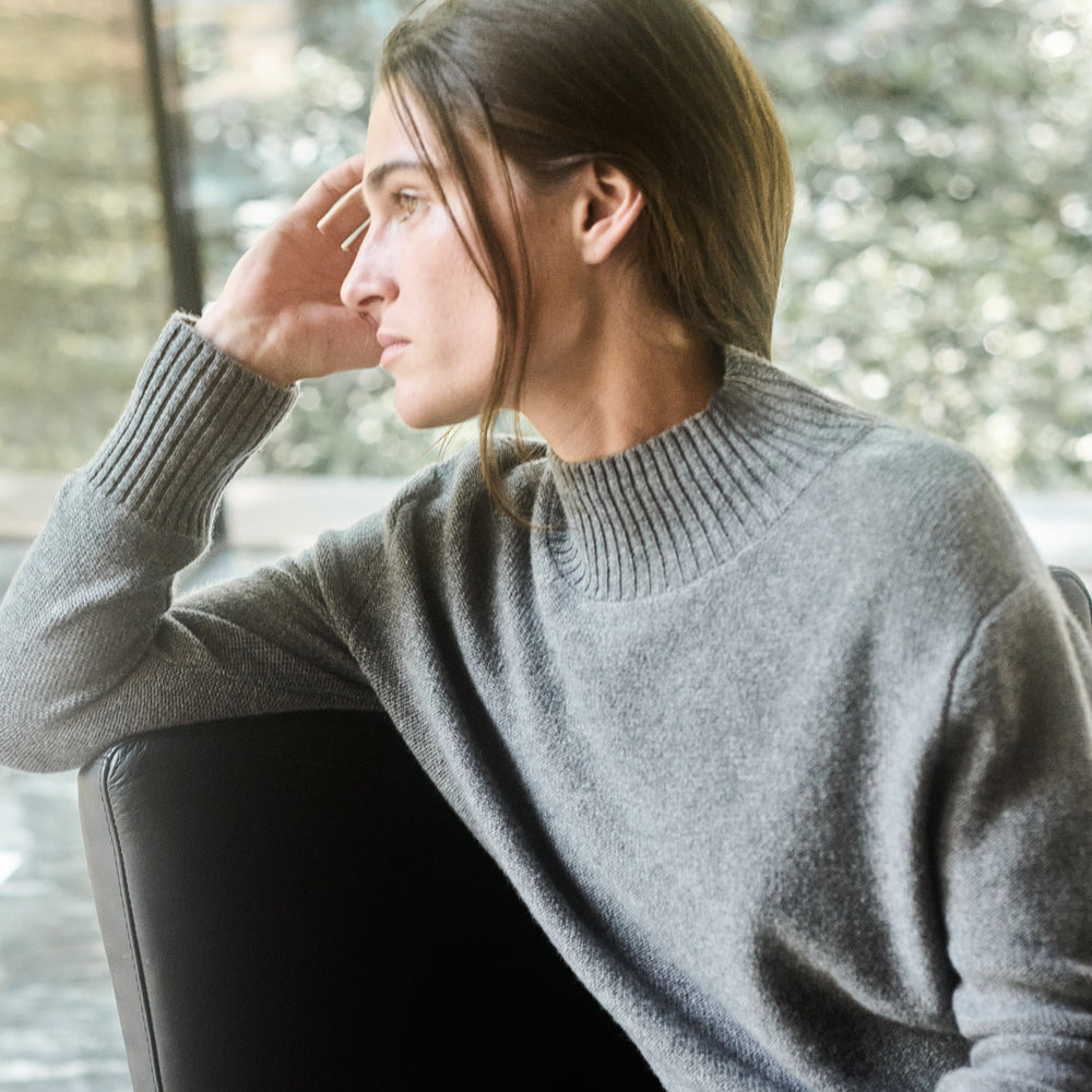 Woman in a gray sweater sitting on a chair with a blurred background