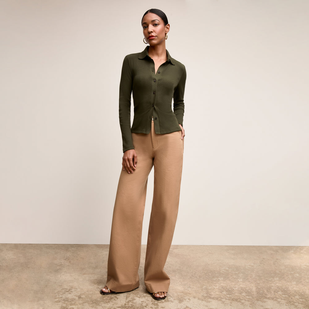 Woman wearing a green cardigan and beige pants against a neutral background