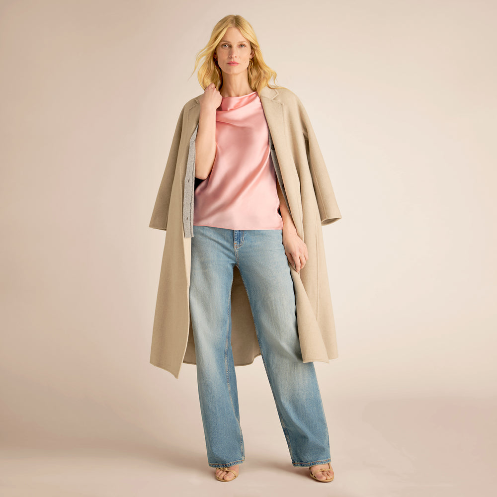 Woman wearing a long beige coat, pink top, and blue jeans on a beige background