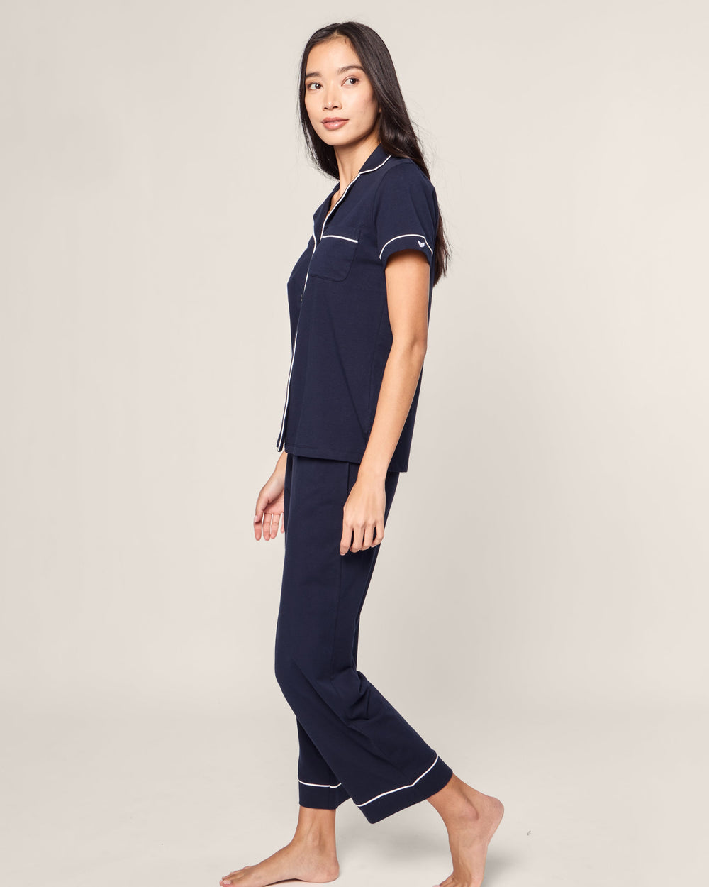 Woman wearing navy blue pajamas with white piping on a beige background