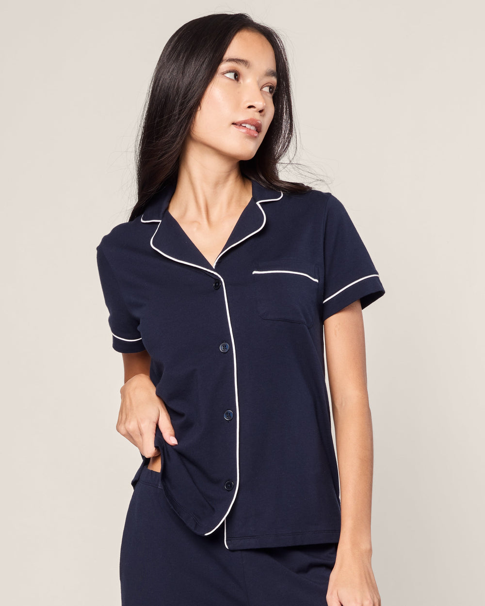 Woman wearing navy pajamas with white piping on a plain background