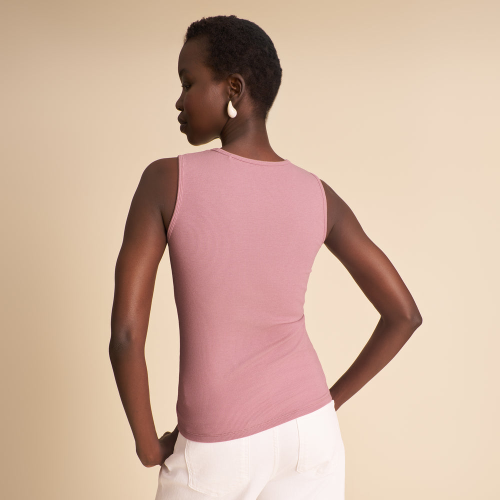 Woman wearing a pink sleeveless top and white pants against a beige background
