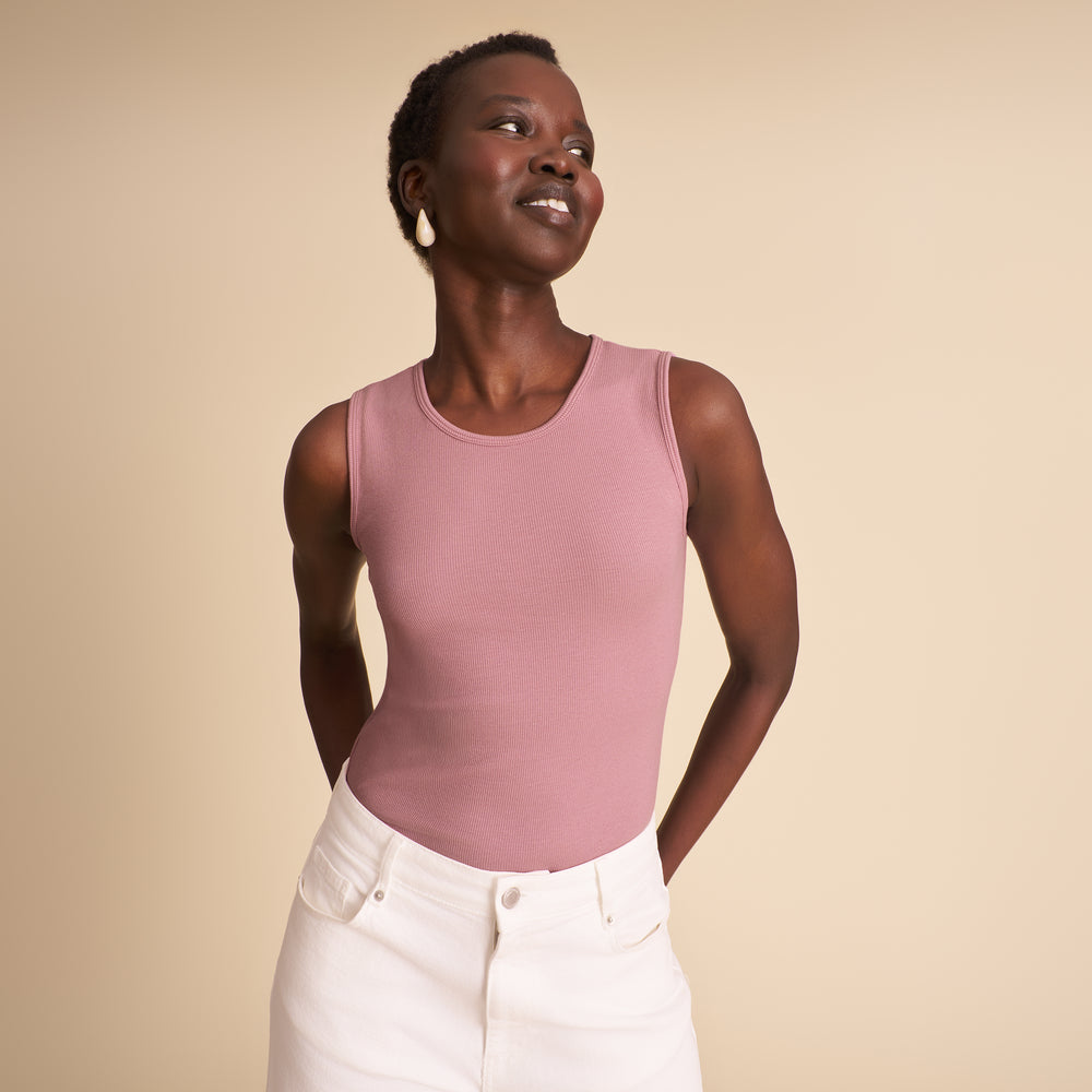 Woman wearing a pink sleeveless top and white pants against a beige background